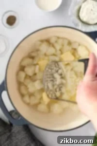 A potato masher mashing potatoes and butter in a Dutch oven.