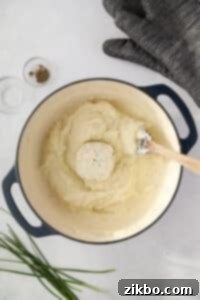 A Dutch oven filled with mashed potatoes, with a round of Boursin cheese placed on top, ready to be mixed in.