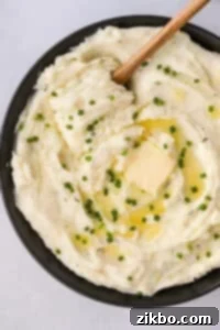 A black bowl filled with creamy Boursin mashed potatoes, topped with melted butter and fresh chopped chives.