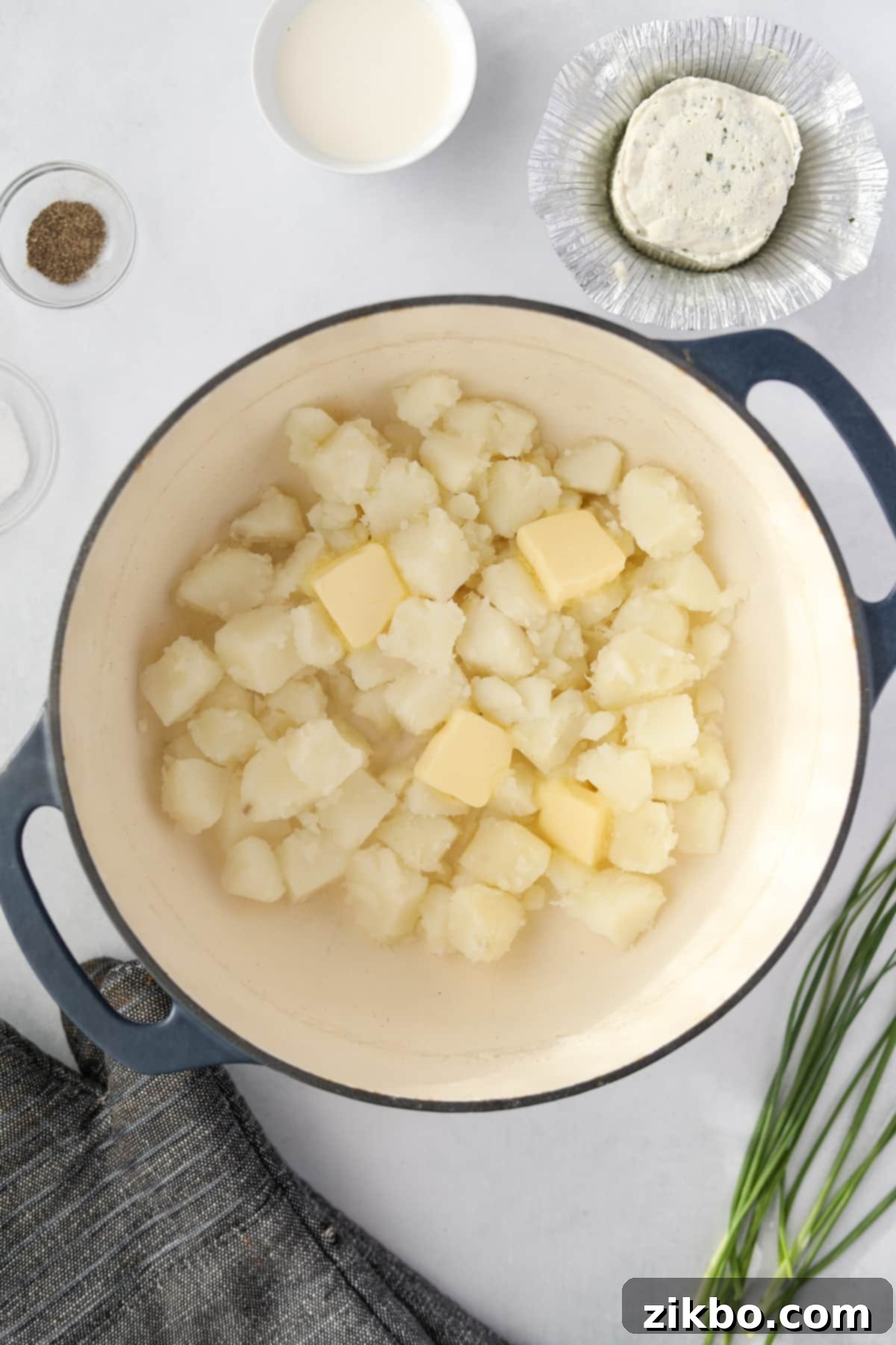 Cooked and drained cubed potatoes with a pat of butter melting in a large pot, steam gently rising.