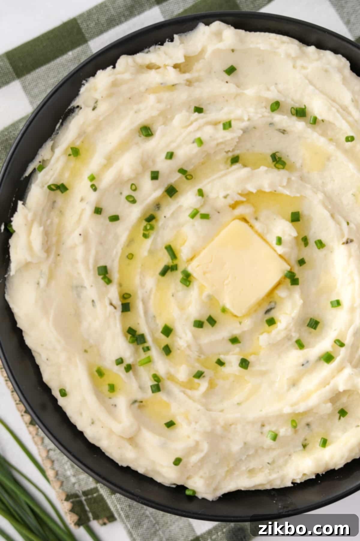 A black bowl brimming with creamy Boursin mashed potatoes, beautifully topped with a melting pat of butter and vibrant fresh chives.