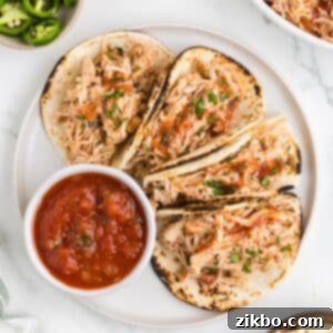 A plate of four folded chicken tacos, with a side of salsa in a small bowl.