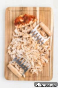Shredding tender chicken breasts on a wooden cutting board with two forks.