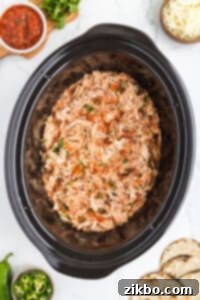A slow cooker filled with perfectly shredded chicken mixed with salsa.