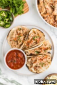 A plate filled with four chicken tacos, beautifully garnished and ready to eat, with a side of salsa.