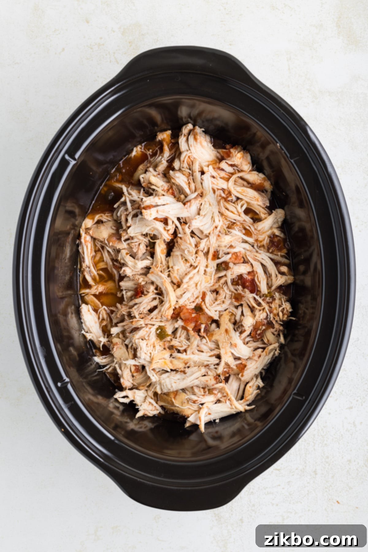 A slow cooker now filled with perfectly shredded salsa chicken, ready to be mixed with the sauce.
