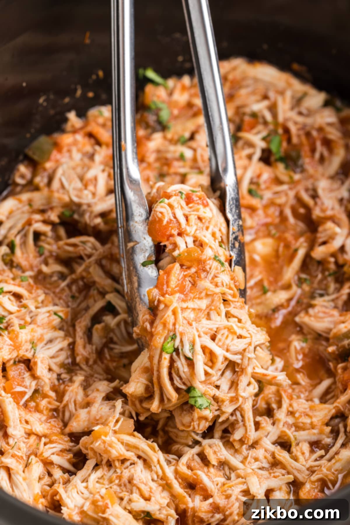 Using a pair of tongs to transfer a generous portion of shredded salsa chicken from a slow cooker, ready to be served.