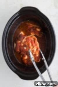 Using tongs to remove salsa chicken from a slow cooker.