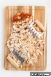 Using meat shredders to shred chicken breasts on a wooden cutting board.