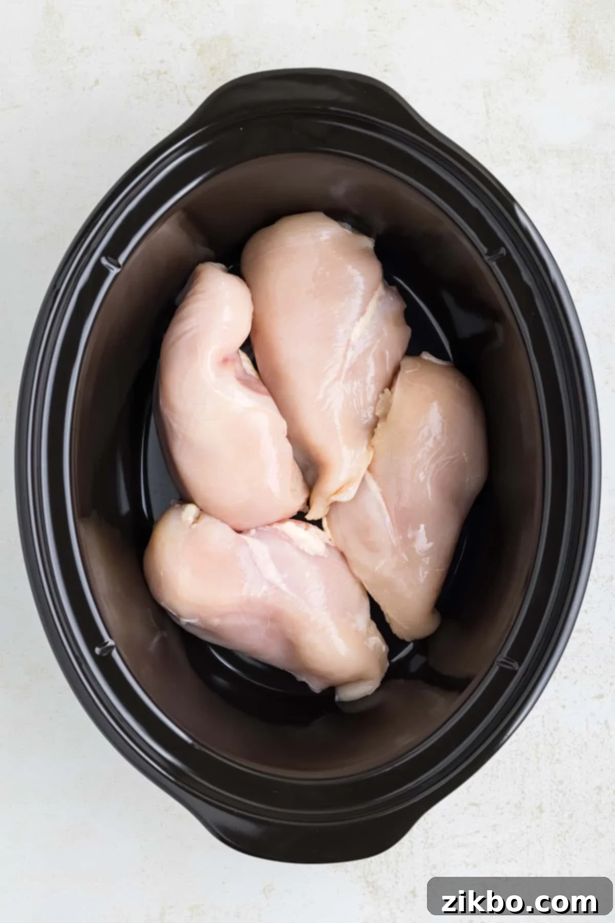 Tender Slow Cooker Salsa Chicken 4 A black slow cooker filled with boneless, skinless chicken breasts arranged in a single layer.