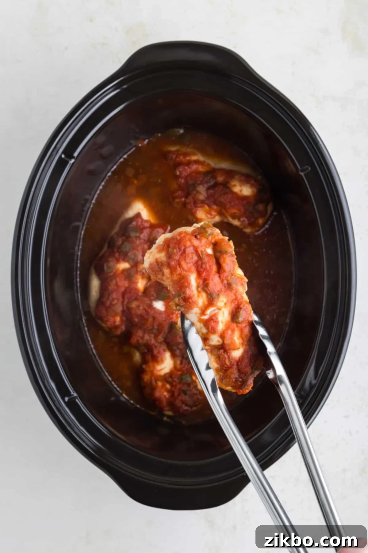 Tender Slow Cooker Salsa Chicken 6 Using tongs to carefully remove a cooked, tender salsa chicken breast from the slow cooker.
