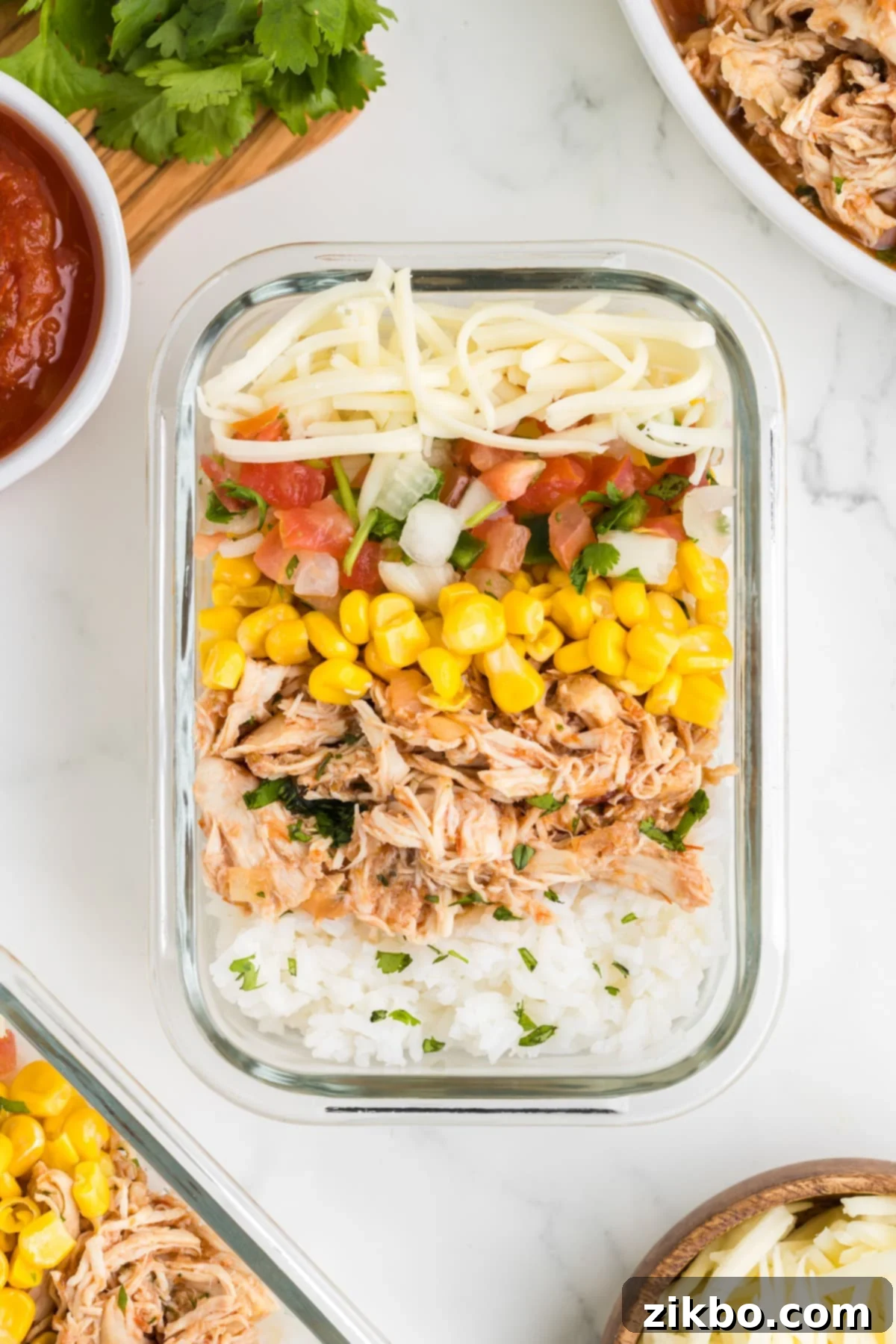 Tender Slow Cooker Salsa Chicken 10 A neatly organized meal prep container, featuring rice, shredded salsa chicken, corn, mixed vegetables, and cheese.