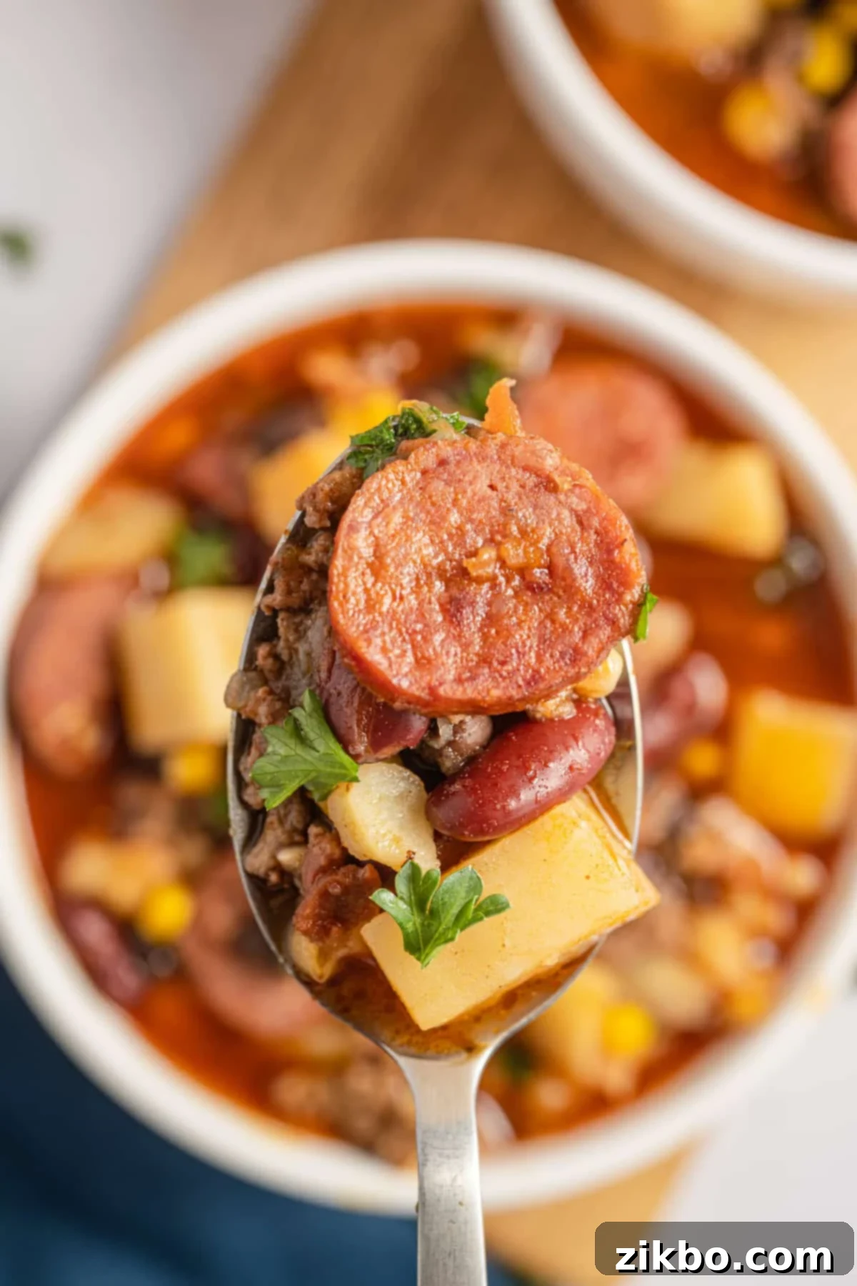 A spoon with Southwestern stew on it, including a smoked sausage round and kidney beans.