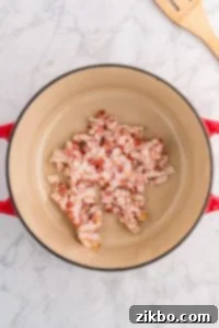 A Dutch Oven filled with raw bacon pieces.