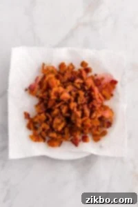 Cooked and crumbled bacon on a paper towel-lined plate.
