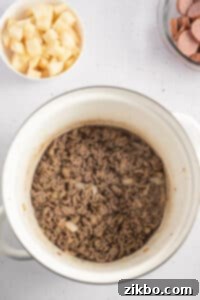 A large soup pot with ground beef that has been cooked inside.