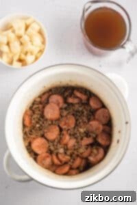 A soup pot filled with ground beef and sliced sausages.