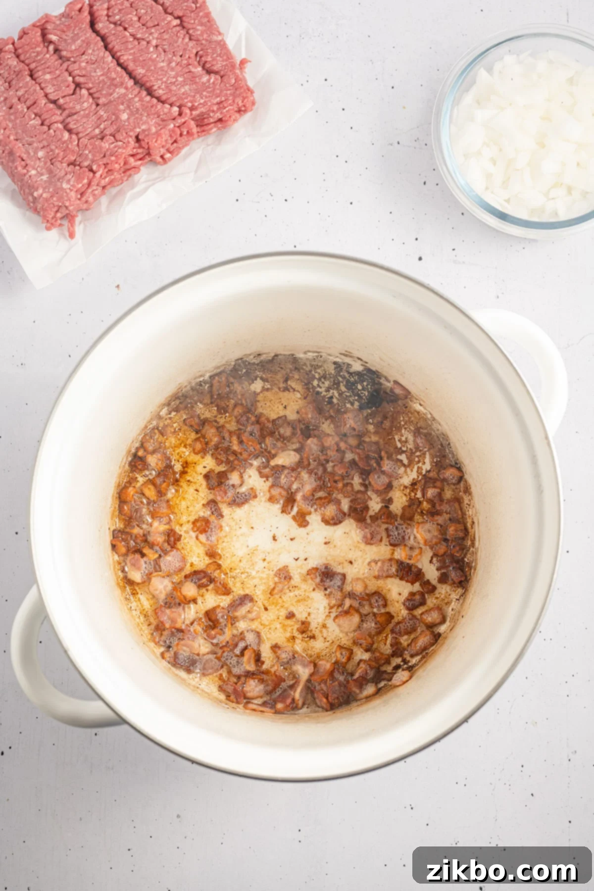 A large pot with onions cooking in bacon fat.