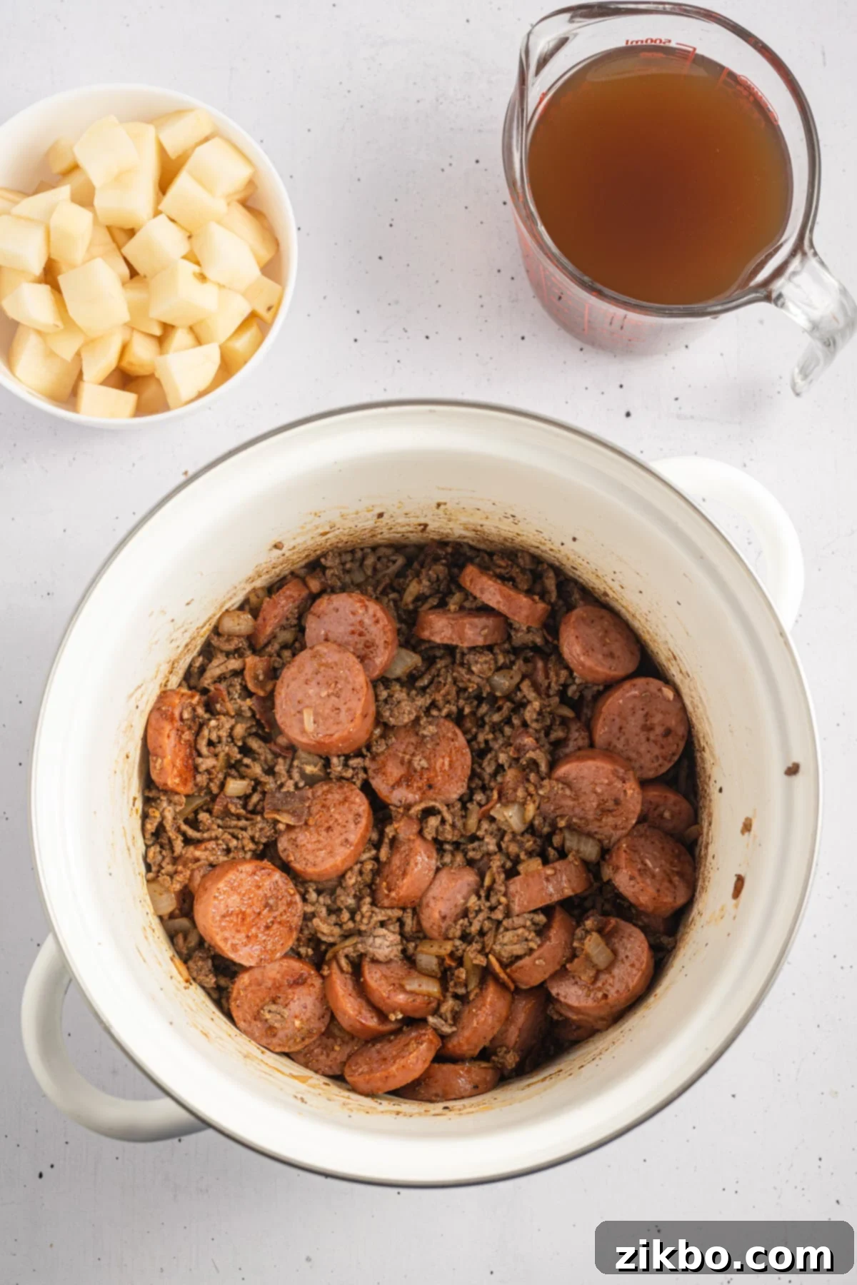A soup pot filled with ground beef and sliced sausages.