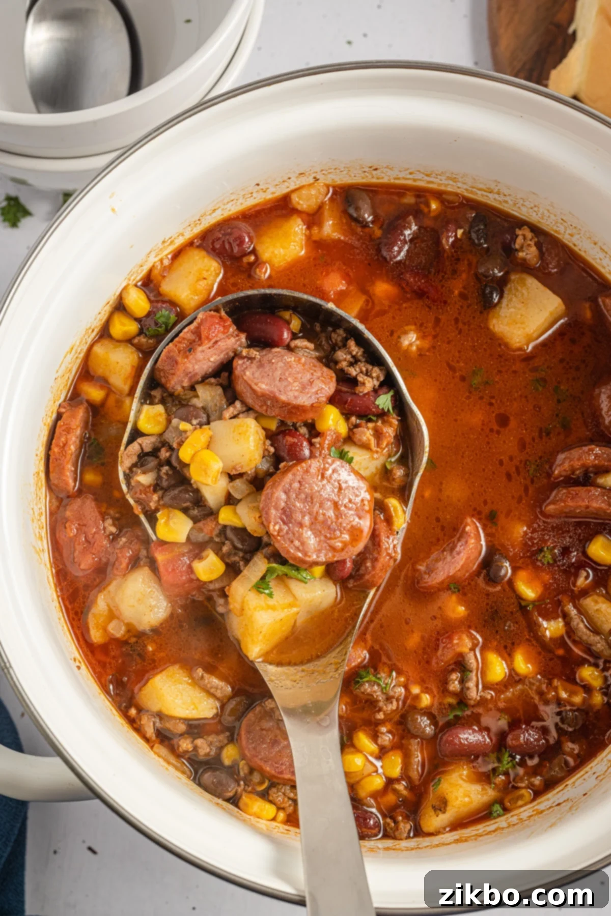 A ladle dipping into a soup pot filled with a Southwestern ground beef stew.