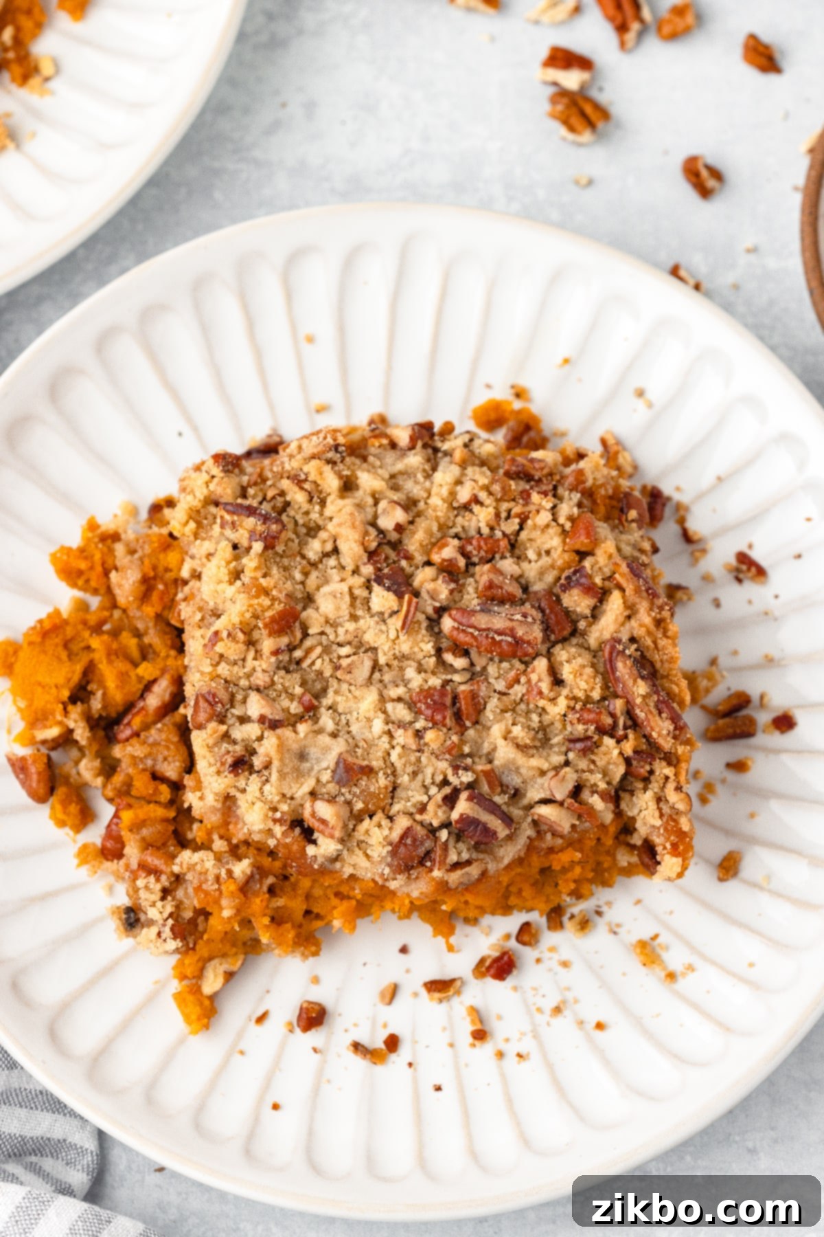A serving of sweet potato casserole on a white plate, showing the creamy texture and pecan topping.