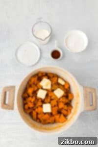 A pot filled with cooked sweet potatoes and a few pats of butter.