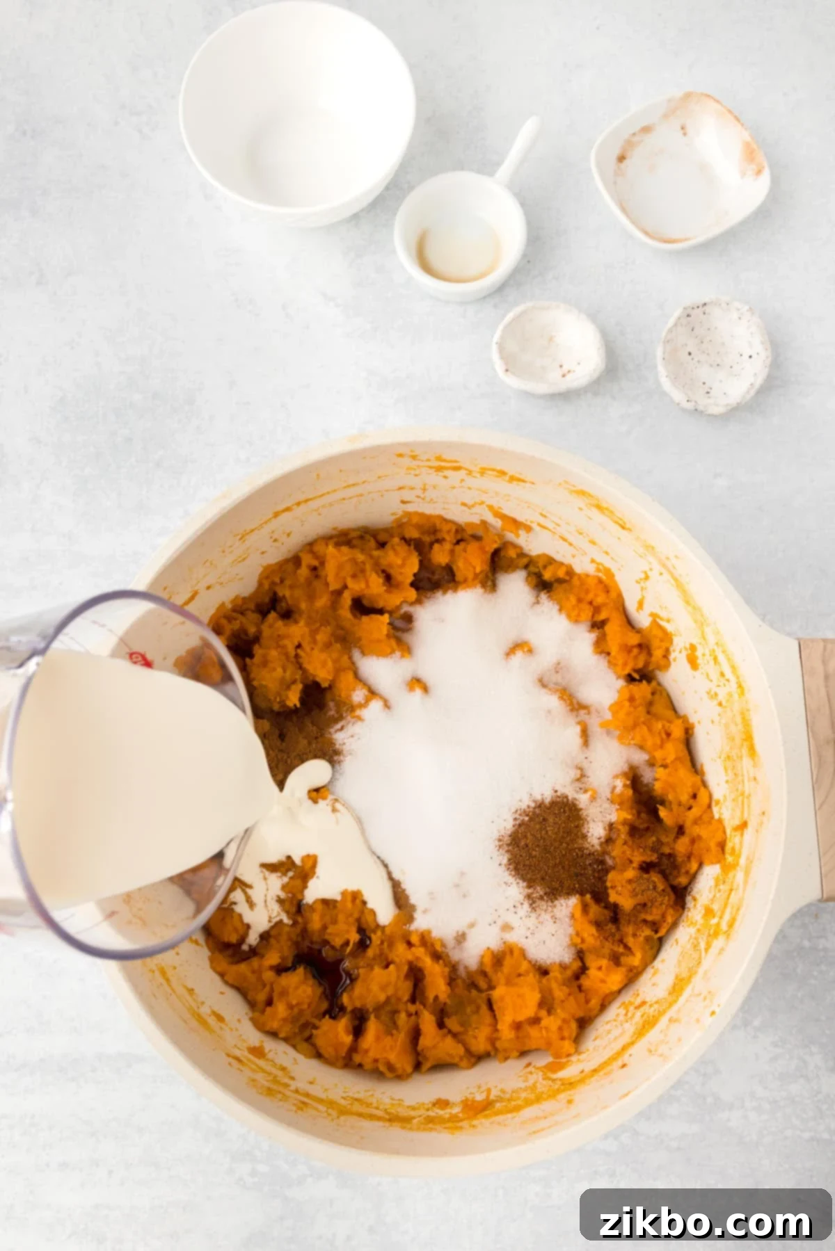A pot of mashed sweet potatoes with sugar, cinnamon, cream, and other spices added, ready for mixing.