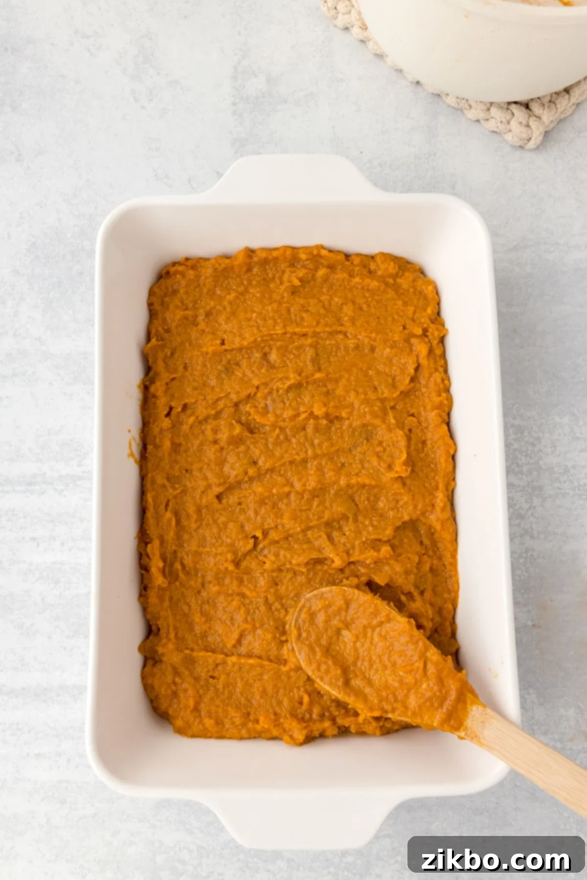Spreading sweet potato casserole mixture evenly into a greased baking dish.