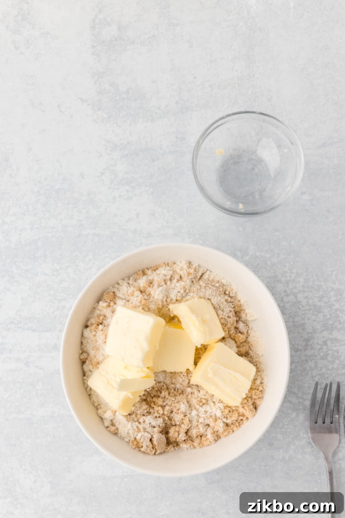 A small bowl of flour and brown sugar with cold butter cubes added, ready for cutting in.
