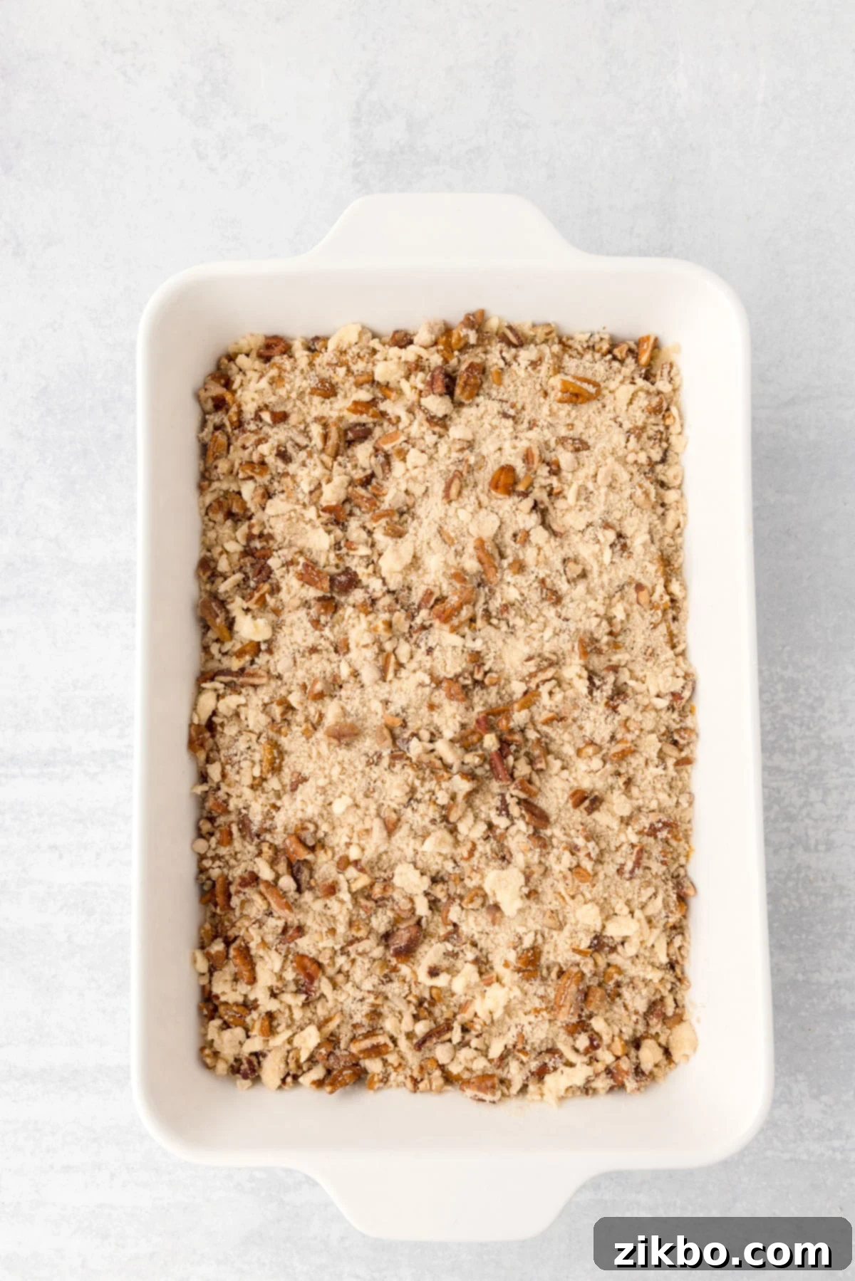 A baking dish filled with an unbaked sweet potato casserole with a pecan crumble topping, ready for the oven.