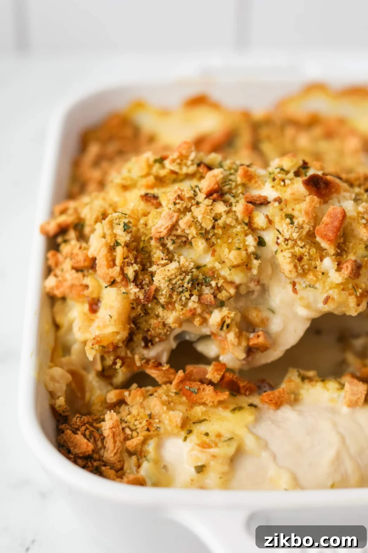 Lifting a chicken breast topped with stuffing mix from a baking dish, showcasing the creamy Swiss Chicken Casserole.