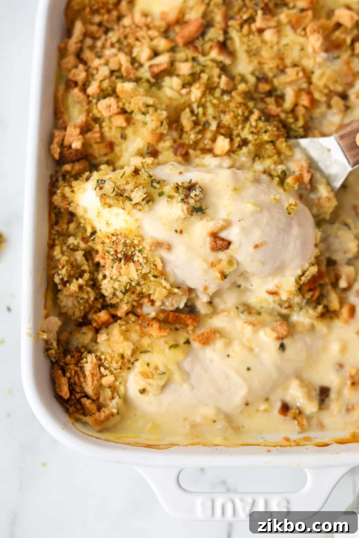 Lifting a tender, cheesy chicken breast from a baking dish of Swiss Chicken Casserole.