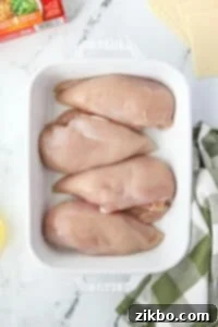 A baking dish with 4 chicken breasts in it.