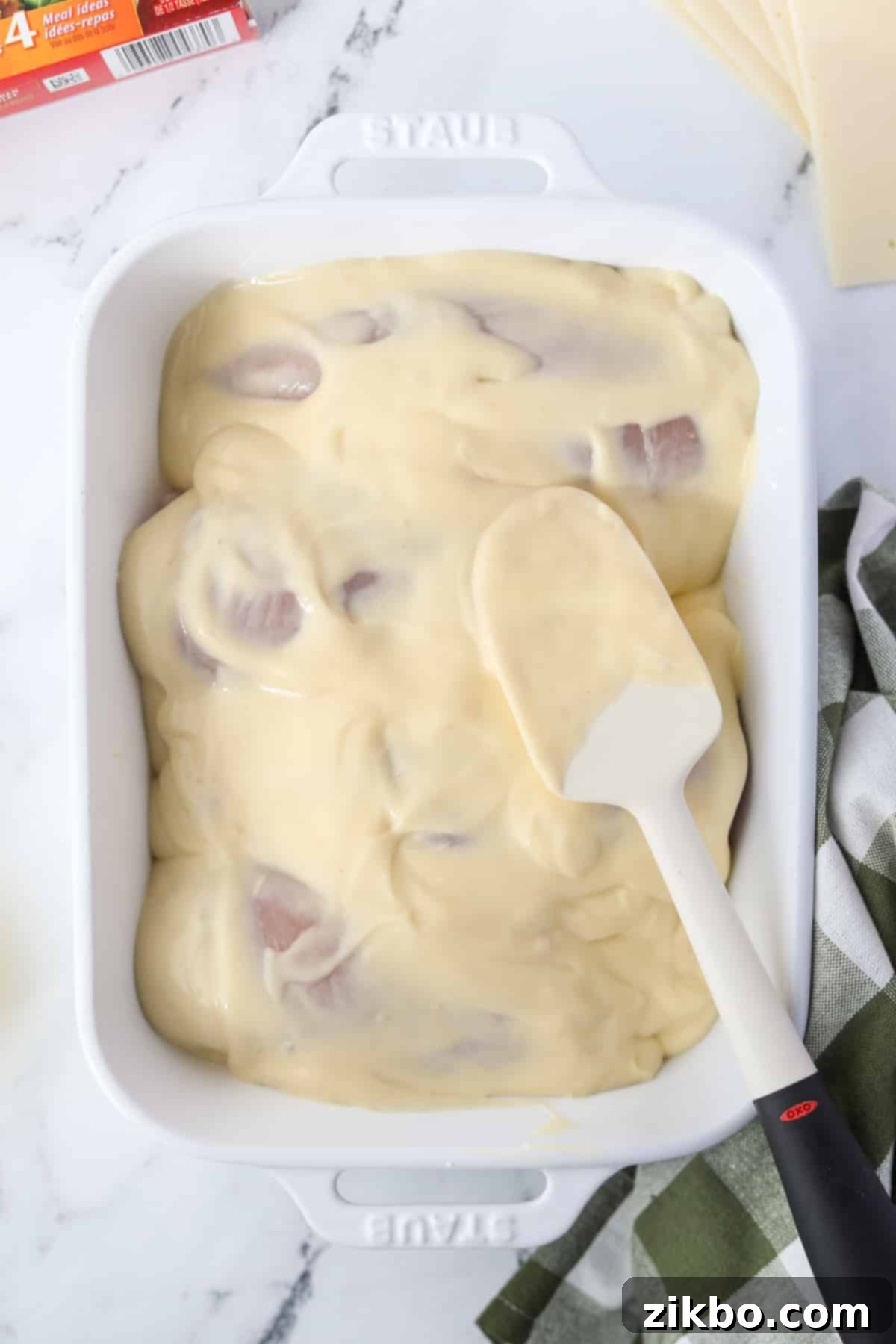 Spreading the creamy soup mixture evenly on top of the raw chicken breasts.