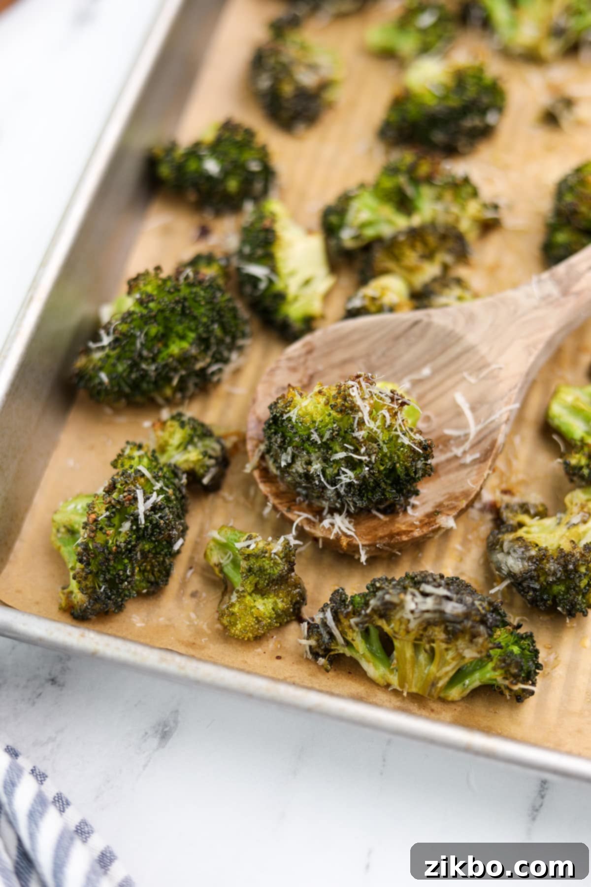 A wooden spoon taking a portion of crispy, golden-brown roasted ranch broccoli from a baking sheet, showcasing its perfect texture.