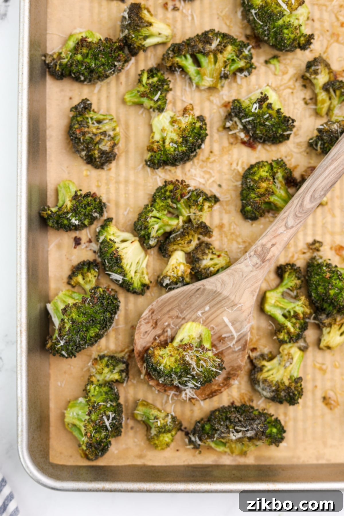 A baking sheet featuring beautifully roasted broccoli florets, generously topped with melted parmesan cheese, glistening and ready to serve.