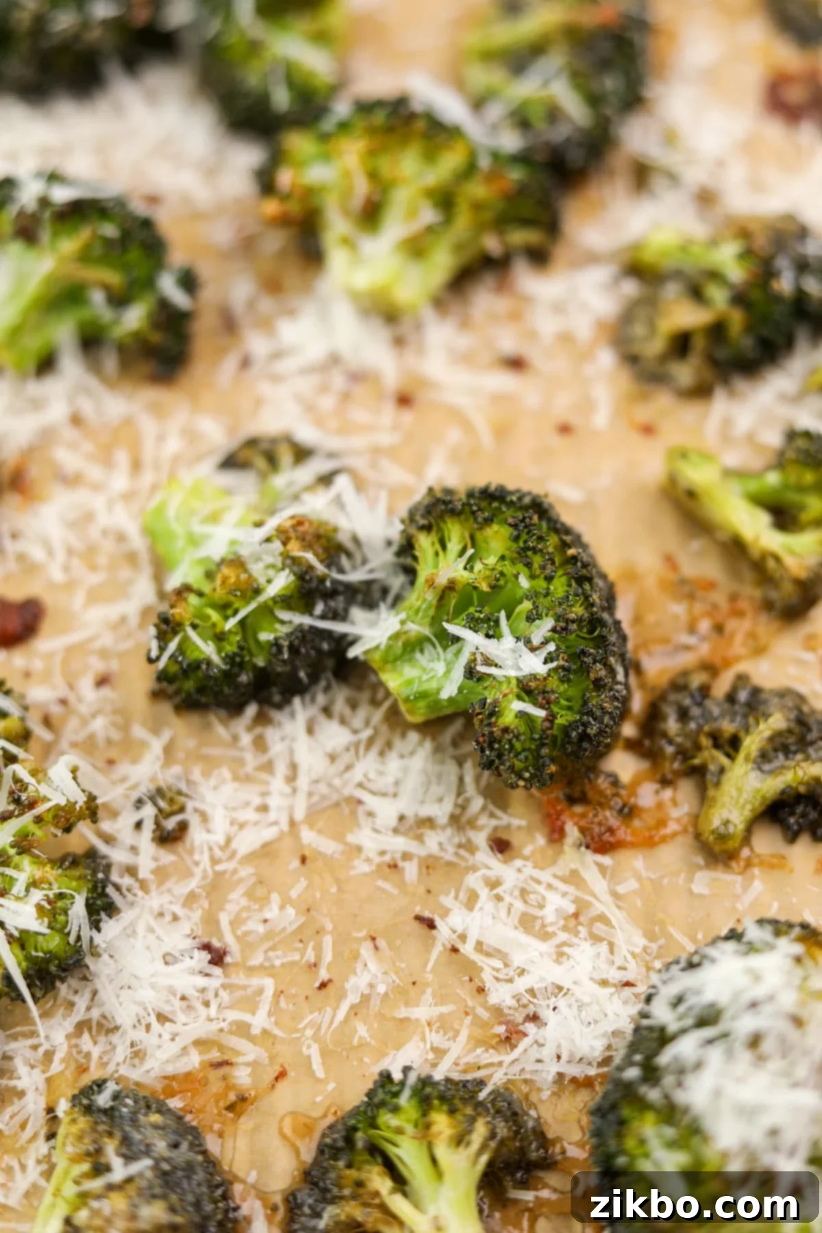 A close-up of roasted broccoli florets, perfectly tender and browned, topped with melted Parmesan cheese, ready to be enjoyed.