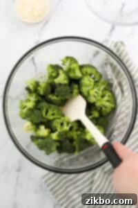 Stirring broccoli into a seasoned oil.