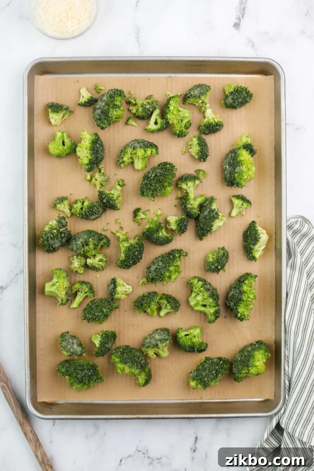 Seasoned broccoli florets spread out in a single layer on a parchment-lined baking sheet, ready for the oven.