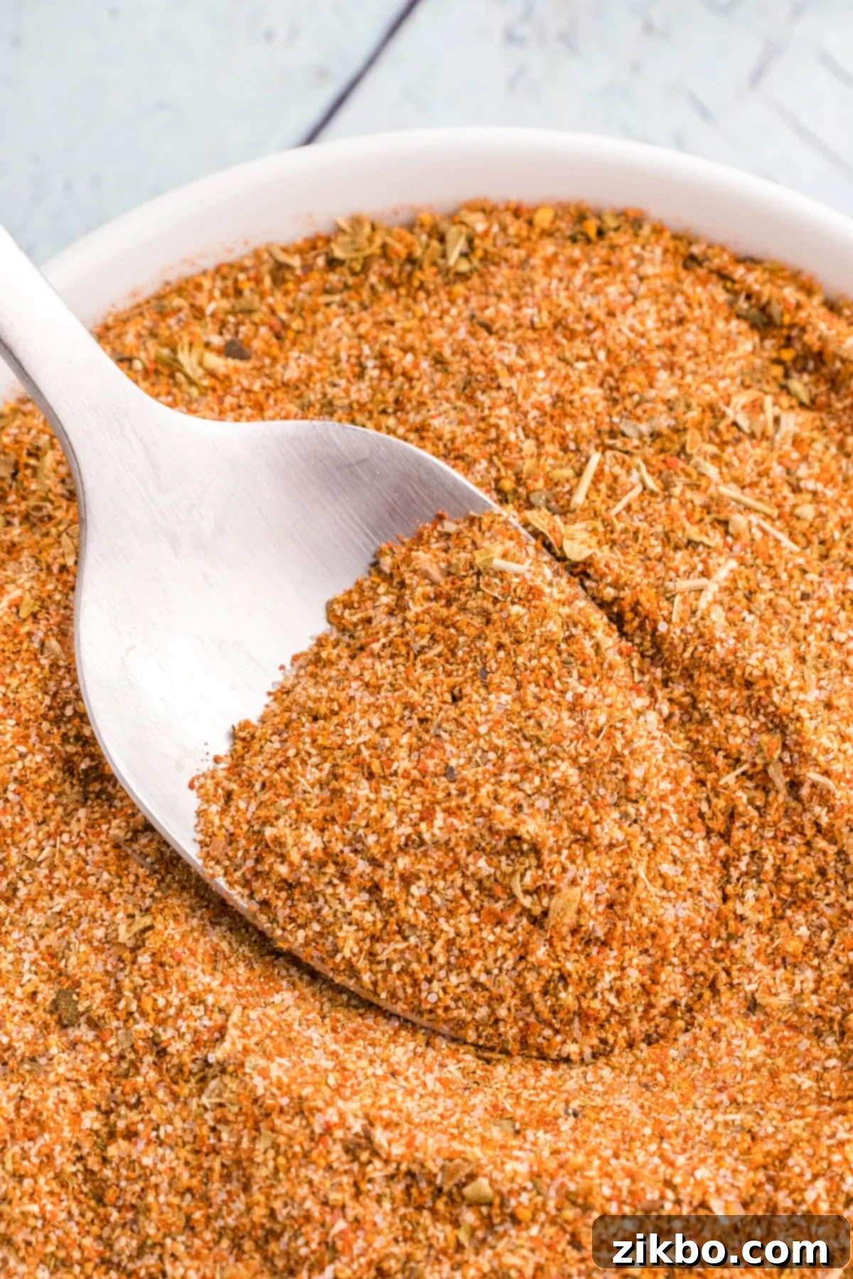 A spoon taking a portion of spice blend from a small white bowl.