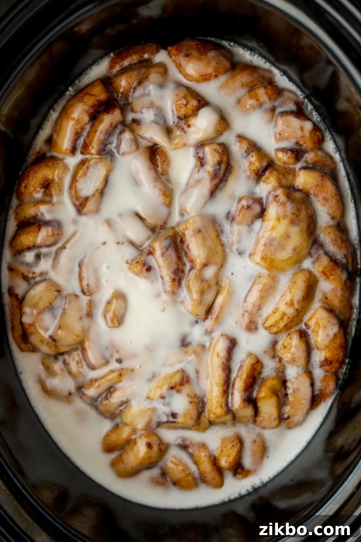 An oval crock pot filled with cinnamon roll casserole topped with plenty of white icing.