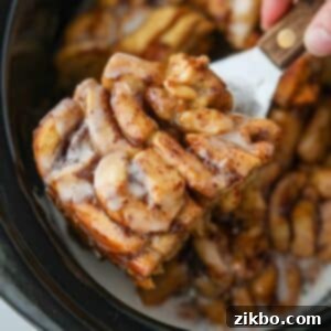 Taking a portion of crock pot cinnamon rolls from a slow cooker. Golden brown cinnamon roll casserole with icing drizzle.