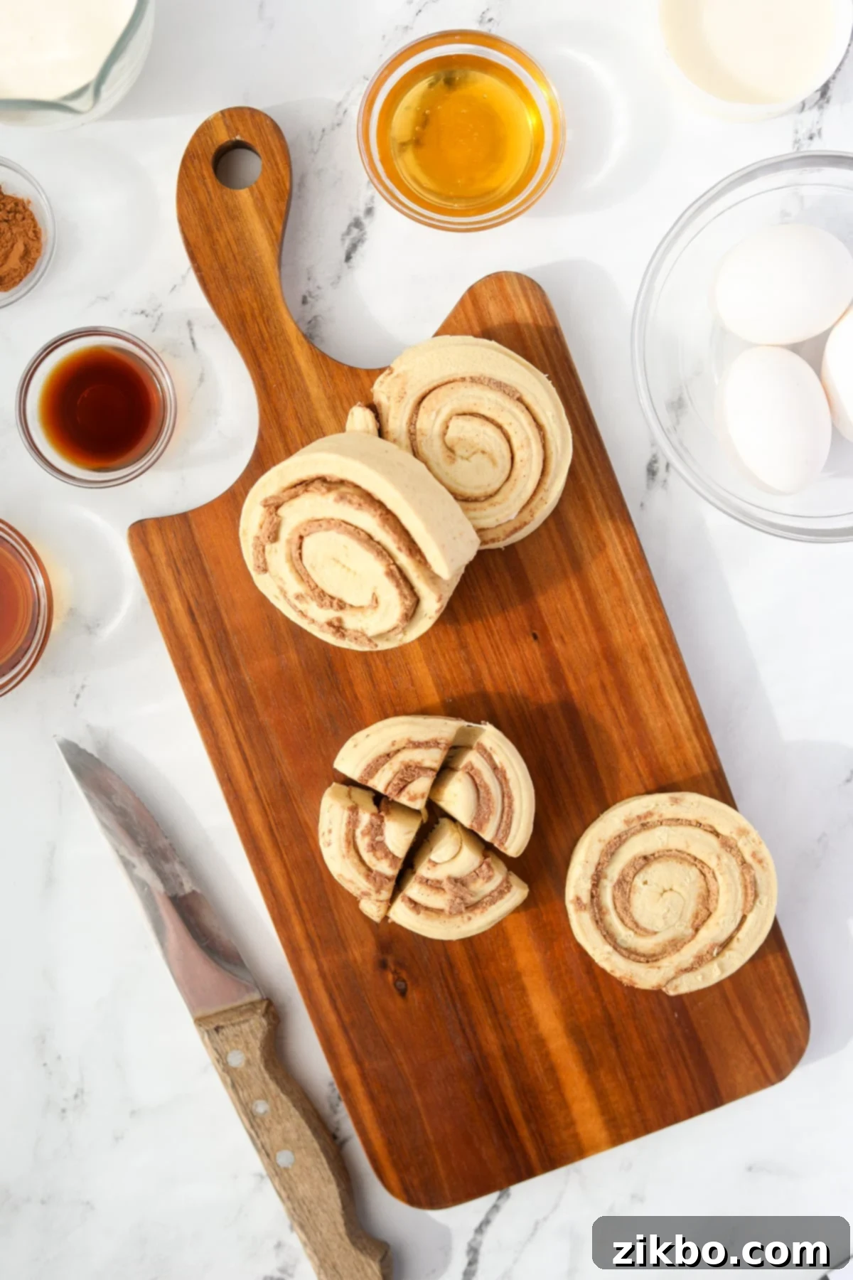 A cutting board with cinnamon rolls being sliced into quarters.