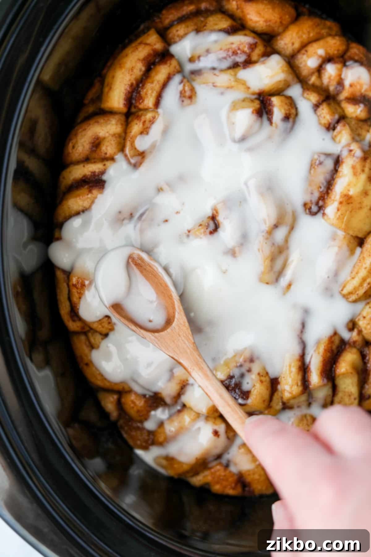 Spreading icing on top of a cinnamon roll casserole inside of a crock pot after cooking.