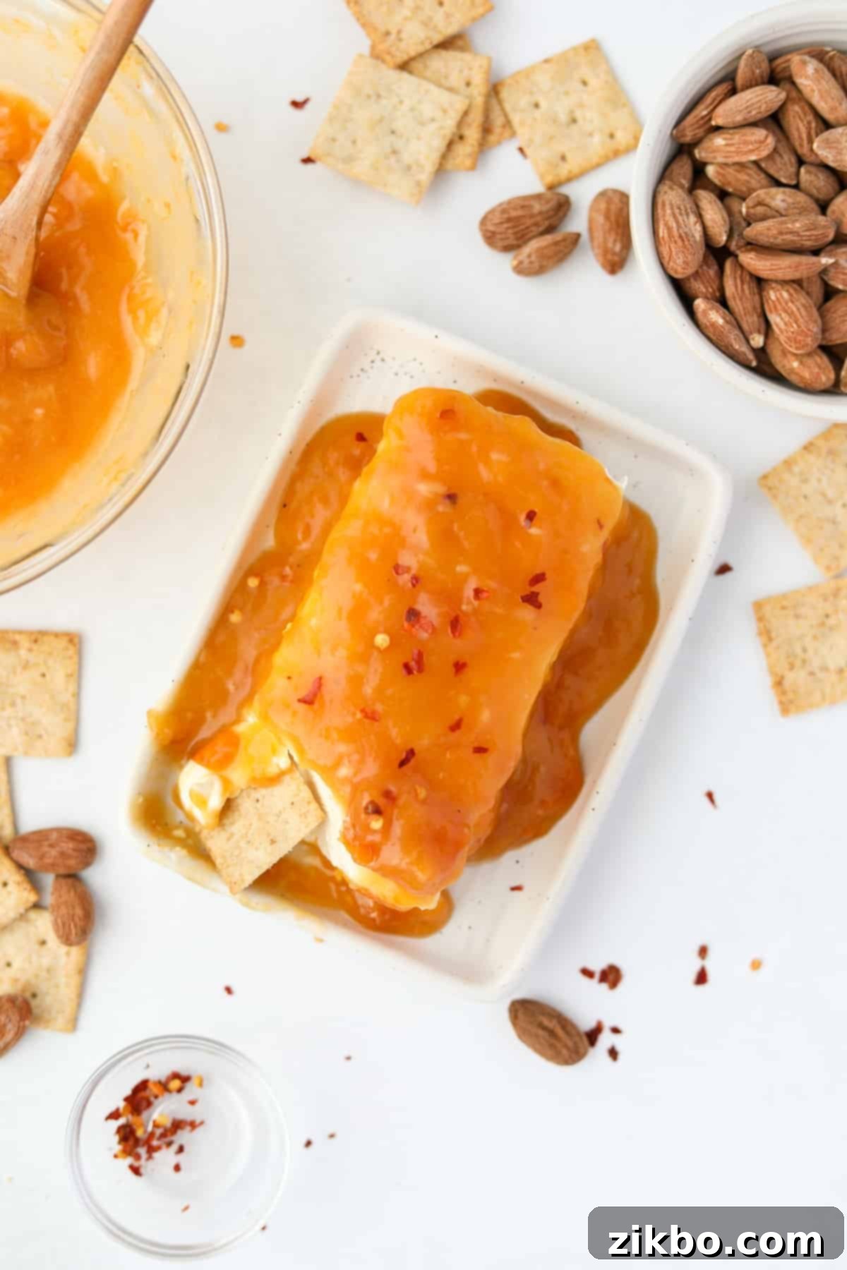 Spicy Southern Jezebel Dip 2 Hot Jezebel Dip served over a block of cream cheese with an assortment of crackers on a wooden board