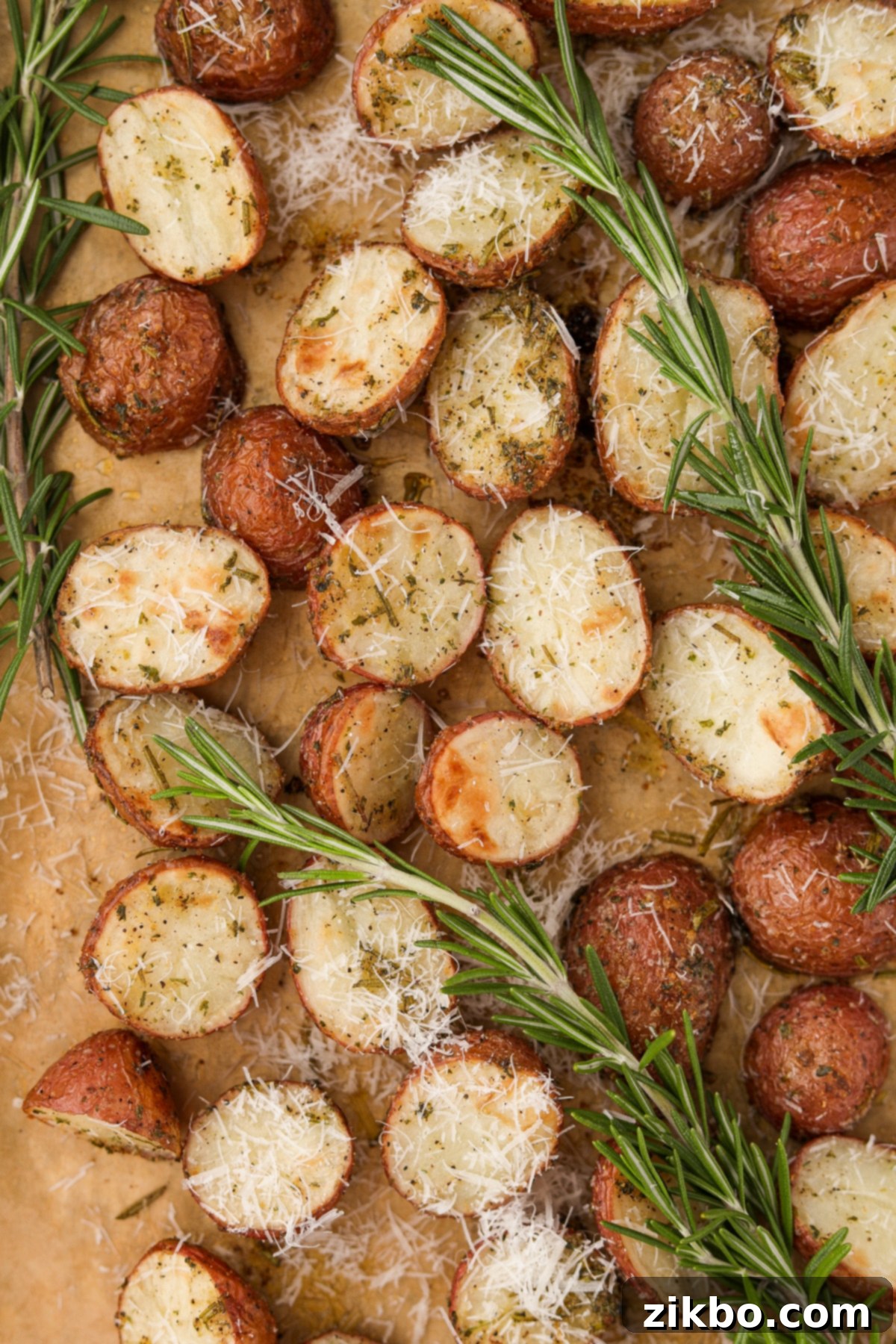 Halved roasted baby potatoes beautifully arranged on a parchment-lined baking sheet, delicately garnished with grated Parmesan cheese and several sprigs of fresh rosemary.