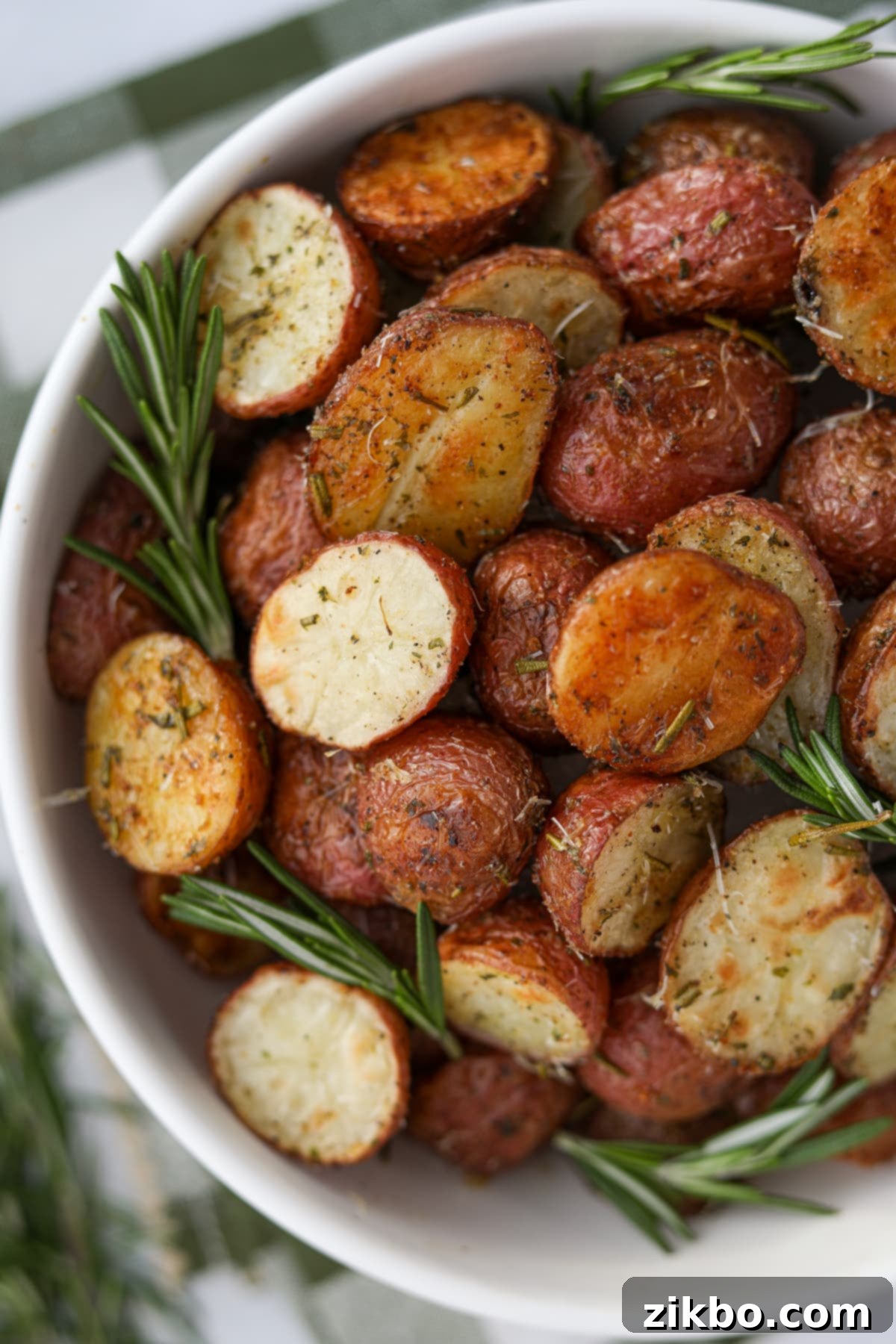 A beautiful bowl showcasing halved, perfectly roasted baby potatoes, generously garnished with several fresh sprigs of rosemary, creating an enticing aroma.