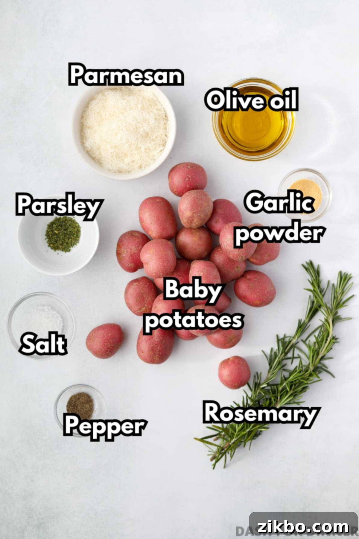 A collection of fresh ingredients laid out: olive oil, coarse salt, black pepper, small baby potatoes, sprigs of rosemary, and garlic powder.