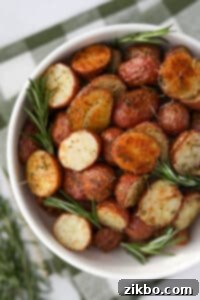 A bowl of roasted potatoes garnished with sprigs of fresh rosemary.