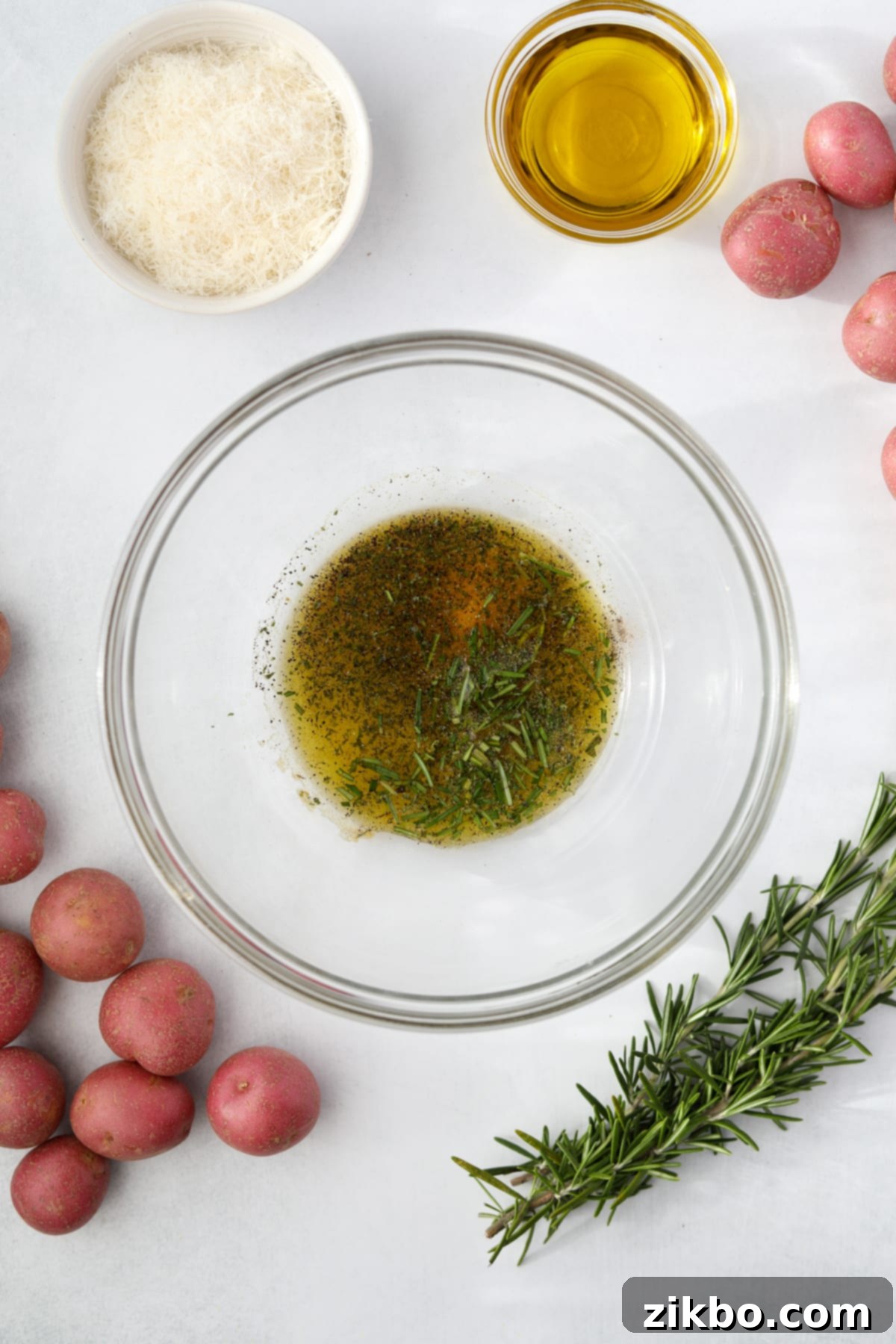 A clear glass bowl containing olive oil mixed with a vibrant blend of fresh and dried herbs and seasonings.